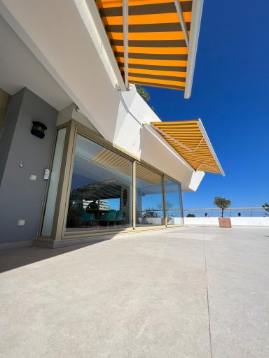 Façade moderne d'un bâtiment avec des stores orange et un ciel bleu clair.