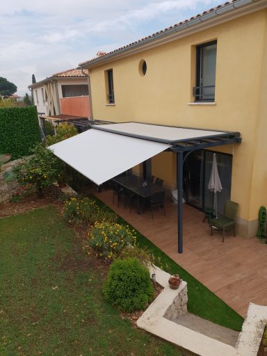 Auvent déplié sur une terrasse ensoleillée près d'une maison jaune.